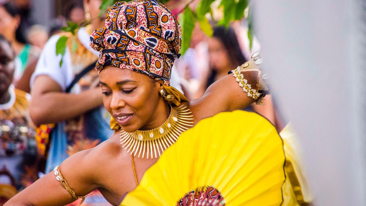 Dançarina afro-brasileira usando trajes coloridos e joias durante uma celebração cultural.