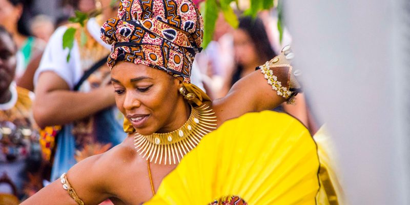 Dançarina afro-brasileira usando trajes coloridos e joias durante uma celebração cultural.