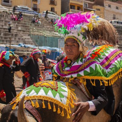 Artista com fantasia colorida montado em um boi durante um festival popular ao ar livre.