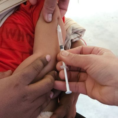 Profissional de saúde aplica uma vacina no braço de uma criança em ambiente interno.