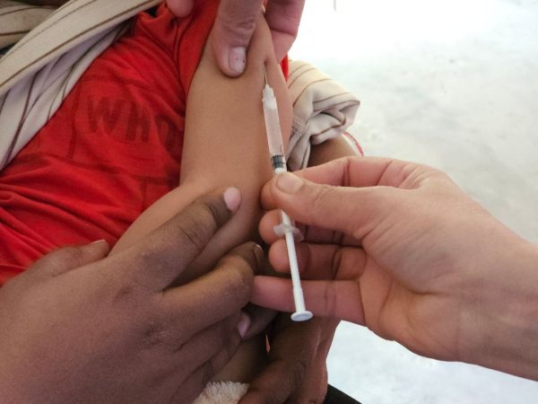 Profissional de saúde aplica uma vacina no braço de uma criança em ambiente interno.