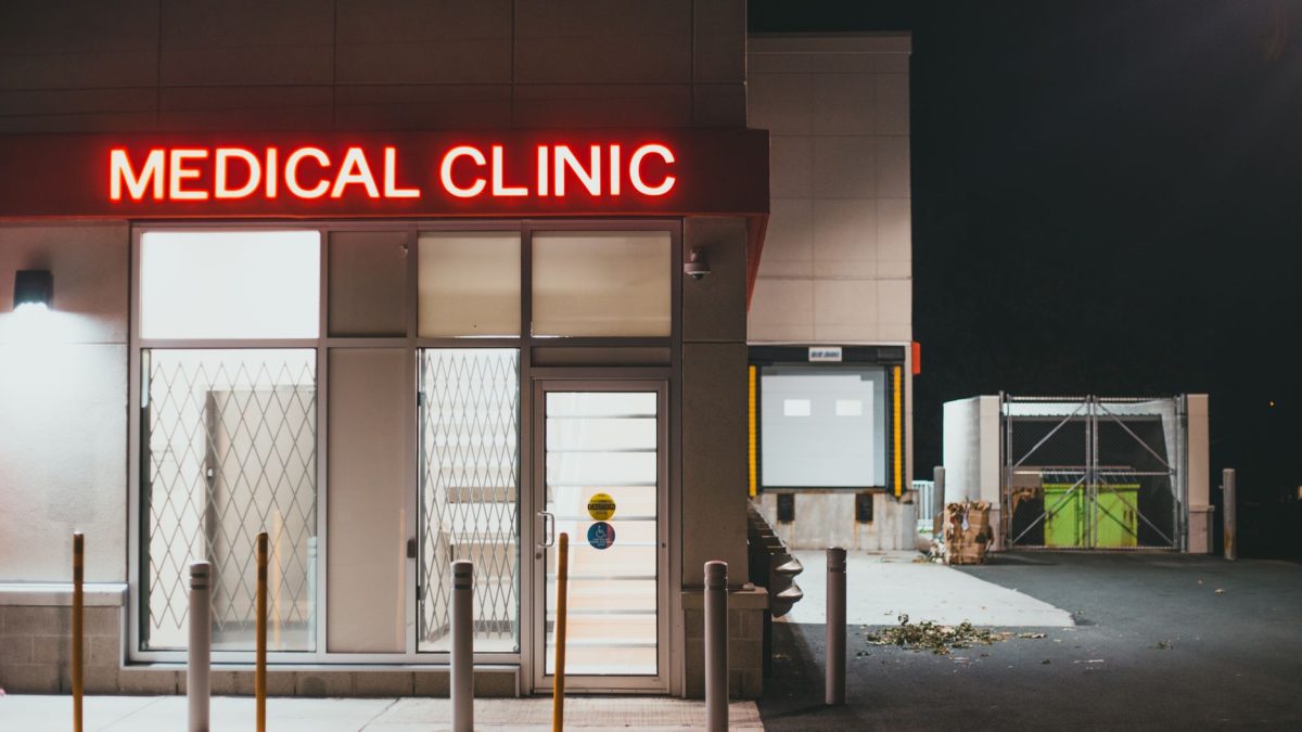 Entrada iluminada de uma clínica médica durante a noite, sem pessoas visíveis.