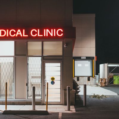 Entrada iluminada de uma clínica médica durante a noite, sem pessoas visíveis.