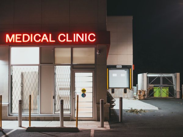 Entrada iluminada de uma clínica médica durante a noite, sem pessoas visíveis.