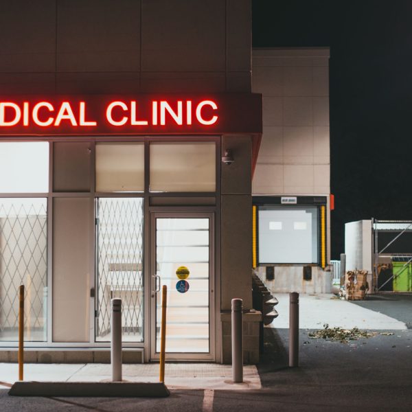 Entrada iluminada de uma clínica médica durante a noite, sem pessoas visíveis.