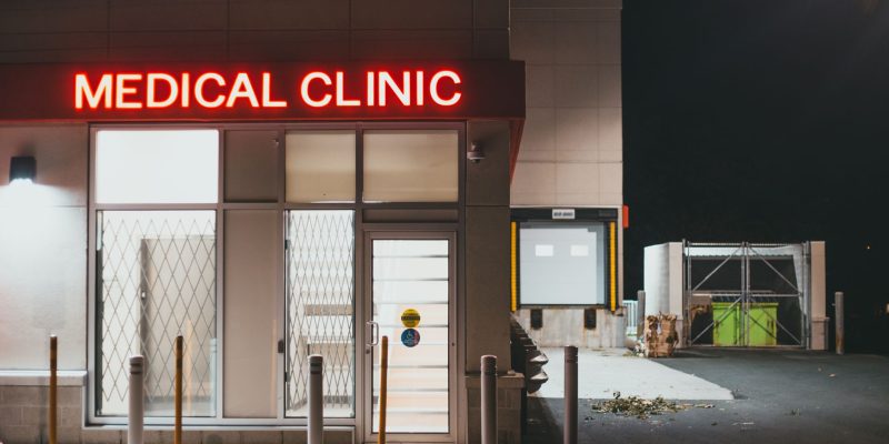 Entrada iluminada de uma clínica médica durante a noite, sem pessoas visíveis.