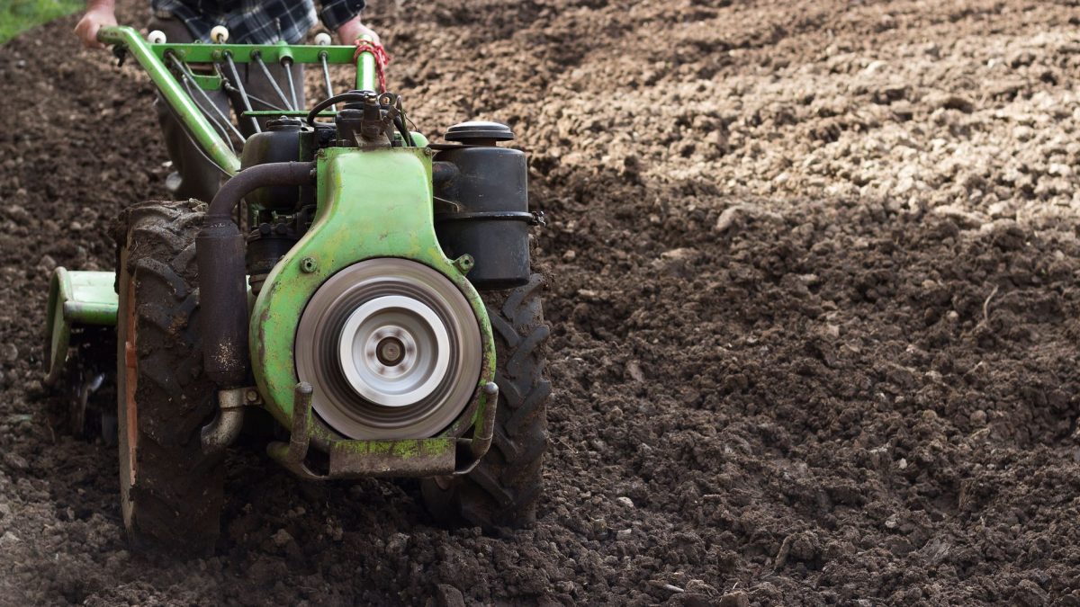 Produtor conduz um trator agrícola de pequeno porte em um campo recém-arado para preparar o solo.