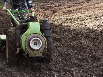 Produtor conduz um trator agrícola de pequeno porte em um campo recém-arado para preparar o solo.