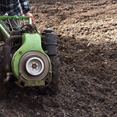 Produtor conduz um trator agrícola de pequeno porte em um campo recém-arado para preparar o solo.