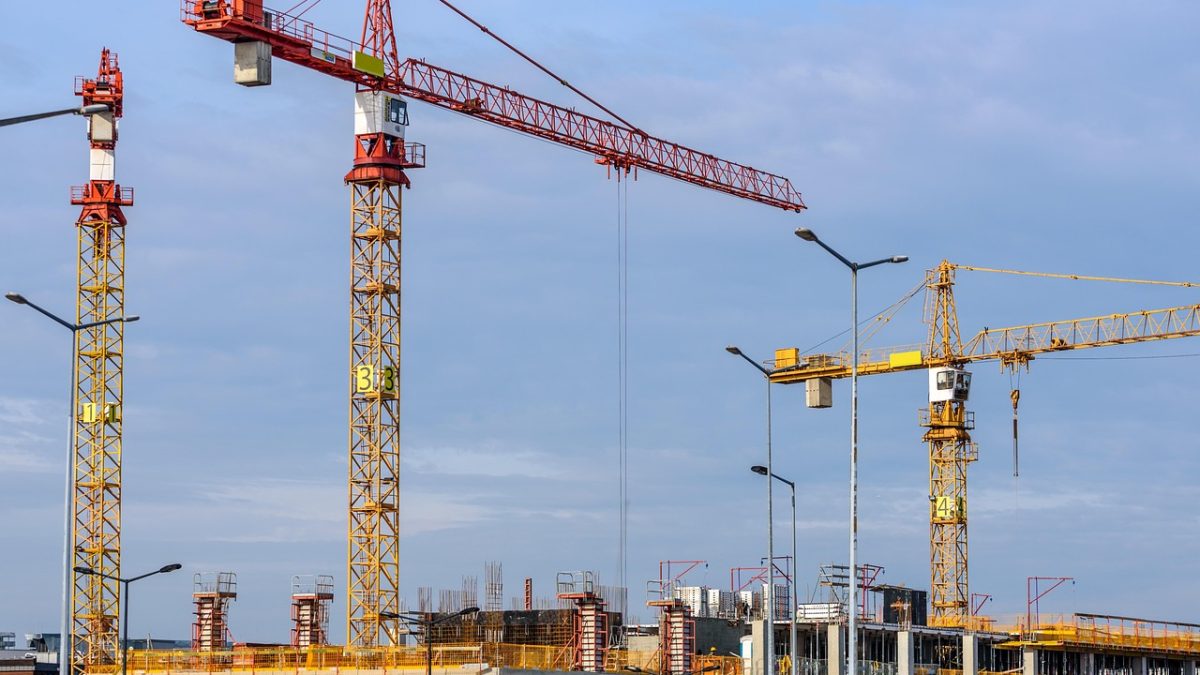 Canteiro de obras com estruturas de concreto, andaimes e guindastes.