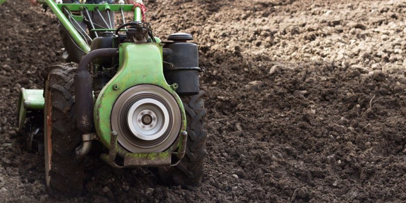 Produtor conduz um trator agrícola de pequeno porte em um campo recém-arado para preparar o solo.